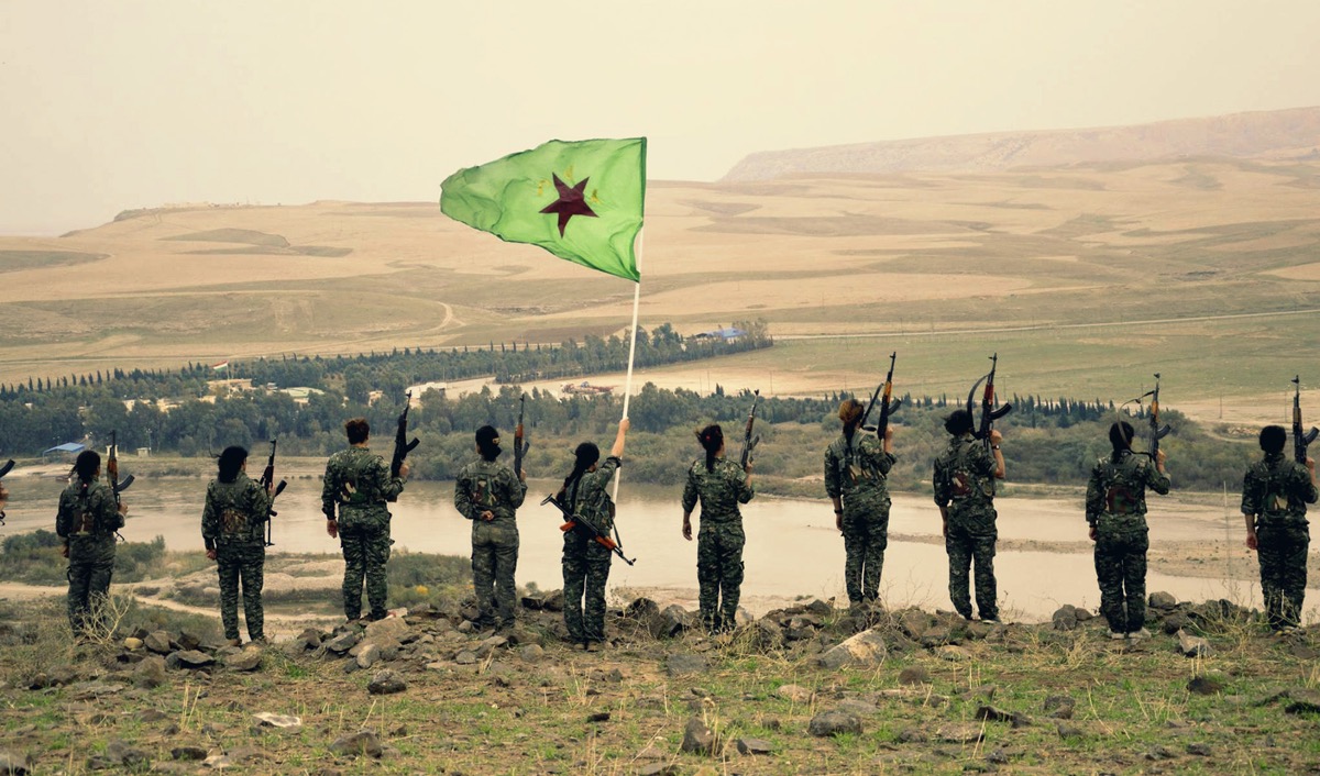 YPJ women fighters standing atop a hill with their flag in Rojava